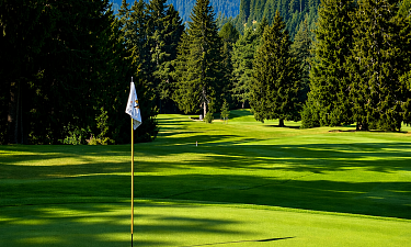 Golfplatz inmitten einer grünen Berglandschaft mit gepflegtem Fairway, umgeben von hohen Bäumen unter blauem Himmel