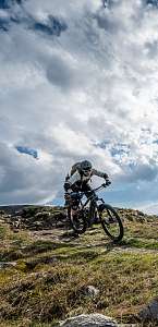 Mountainbiker auf einem alpinen Trail in der Lenzerheide unter dramatischem Himmel mit Sonnenstrahlen