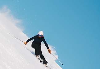 Skier descending a steep slope against a bright blue sky – skiing in Lenzerheide.