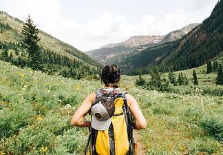 Hiker with a yellow backpack gazing across a sweeping mountain landscape with forests, meadows and peaks – hiking holiday in the mountains.